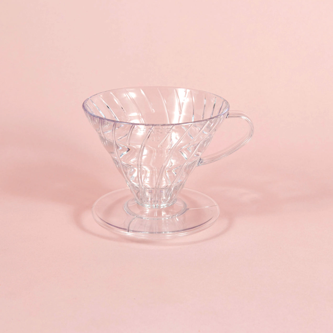 Clear, plastic coffee pour over sitting in the middle of a light pink background. Available through the Awesome Coffee Club.